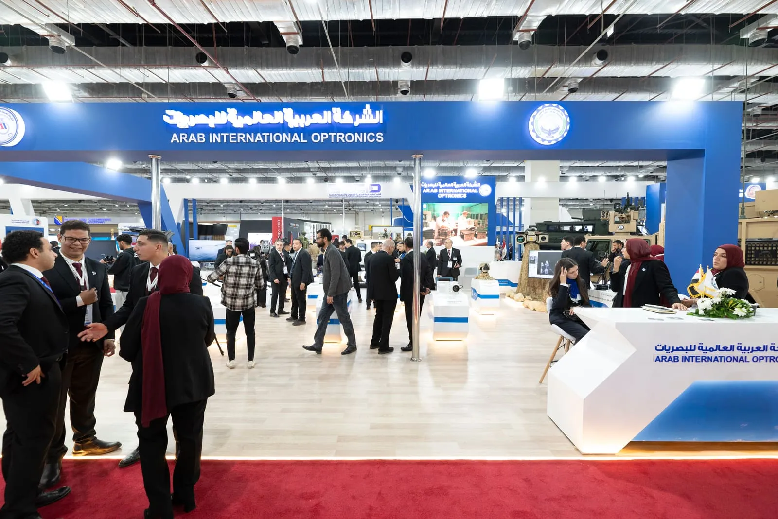 Visitors crowding an exhibition stand on a red-carpet aisle